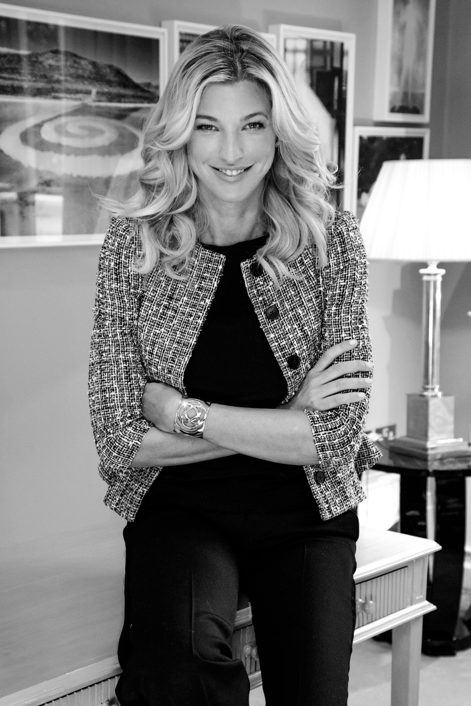 Black and white portrait of Nicole Junkerman smiling, seated on the edge of a table in a bright room.