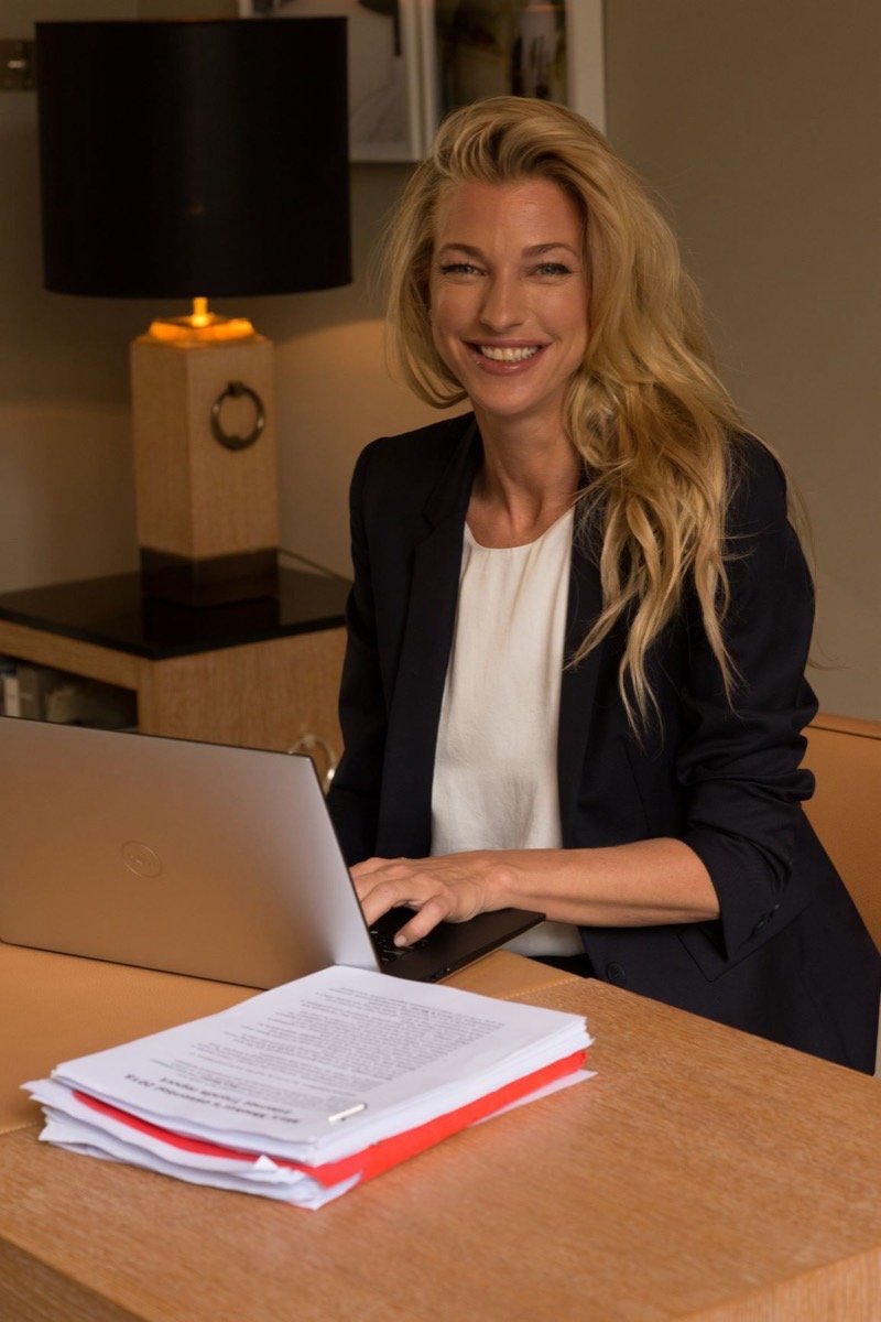 Nicole Junkerman smiling as she writes at a lamp-lit desk with a laptop and open notebook.