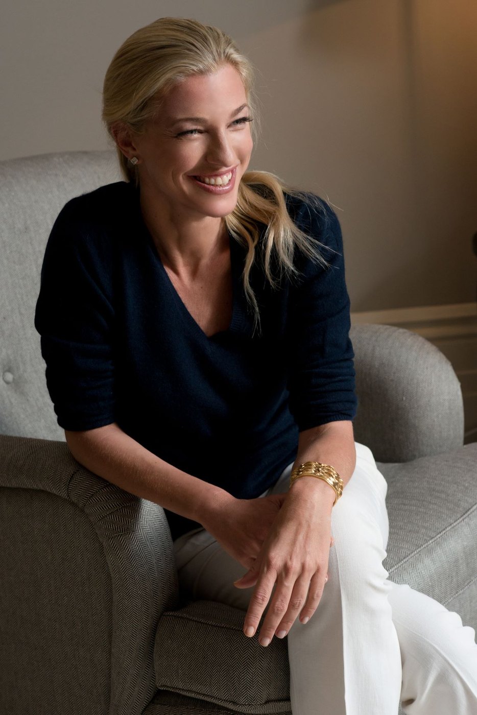 Nicole Junkerman smiling in a navy jumper, seated in a soft armchair at home.